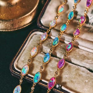May include: A gold chain bracelet featuring a series of marquise-cut opals that display iridescent flashes of blue, green, and pink. The stones are set in gold metal frames and connected by small, round, clear accent stones along the chain.