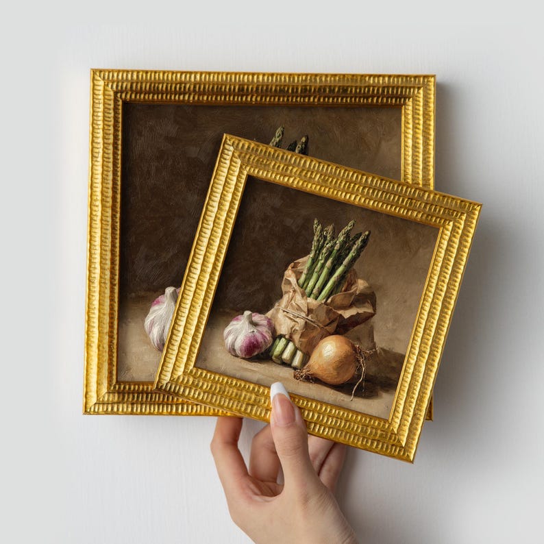 May include: Two framed still life paintings featuring asparagus in a paper bag, garlic, and an onion. The frames are gold with a textured design. The paintings have a warm color palette with brown and beige tones.