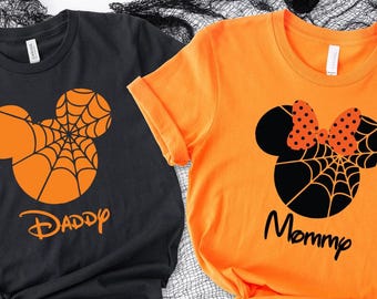 May include: A black t-shirt with an orange spiderweb Mickey Mouse silhouette and the text Daddy, and an orange t-shirt with a black spiderweb Minnie Mouse silhouette featuring a polka dot bow and the text Mommy.
