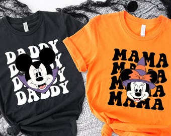 May include: Two short-sleeved t-shirts. One is black with a Mickey Mouse graphic and the word "DADDY" repeated. The other is orange with a Minnie Mouse graphic and the word "MAMA" repeated. Both shirts have a Halloween theme.