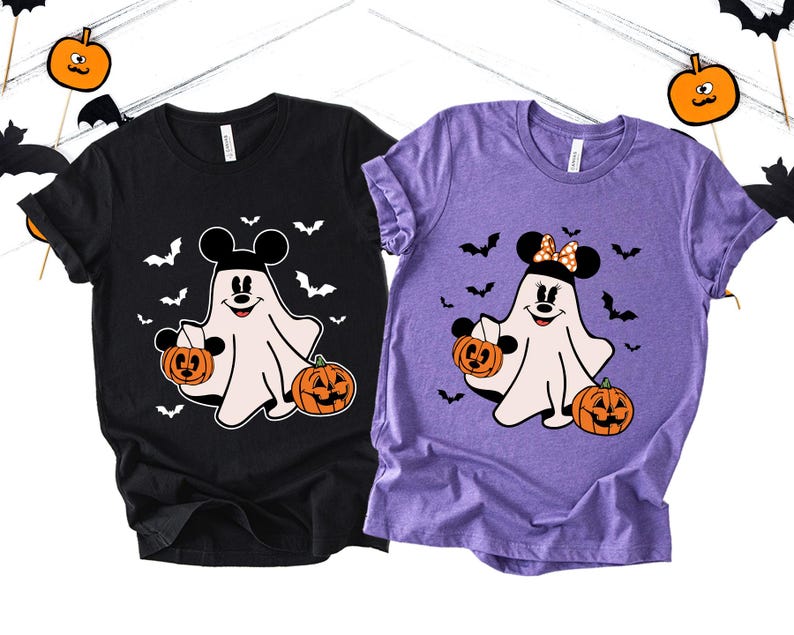May include: A black t-shirt and a purple t-shirt, each featuring a white ghost graphic wearing mouse ears. The ghost on the black shirt wears plain black ears, while the ghost on the purple shirt wears polka-dot ears. Both hold orange jack-o'-lanterns.