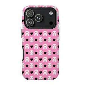 May include: Pink phone case with a repeating pattern of white skulls and black hearts. The case has a black camera module and a black border. The design is a playful and edgy aesthetic.