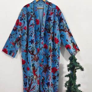 May include: A long, open-front robe in a vibrant blue hue, adorned with a detailed floral and bird pattern in red and brown. The robe is hanging on a wooden hanger against a white background, showcasing its flowing design.