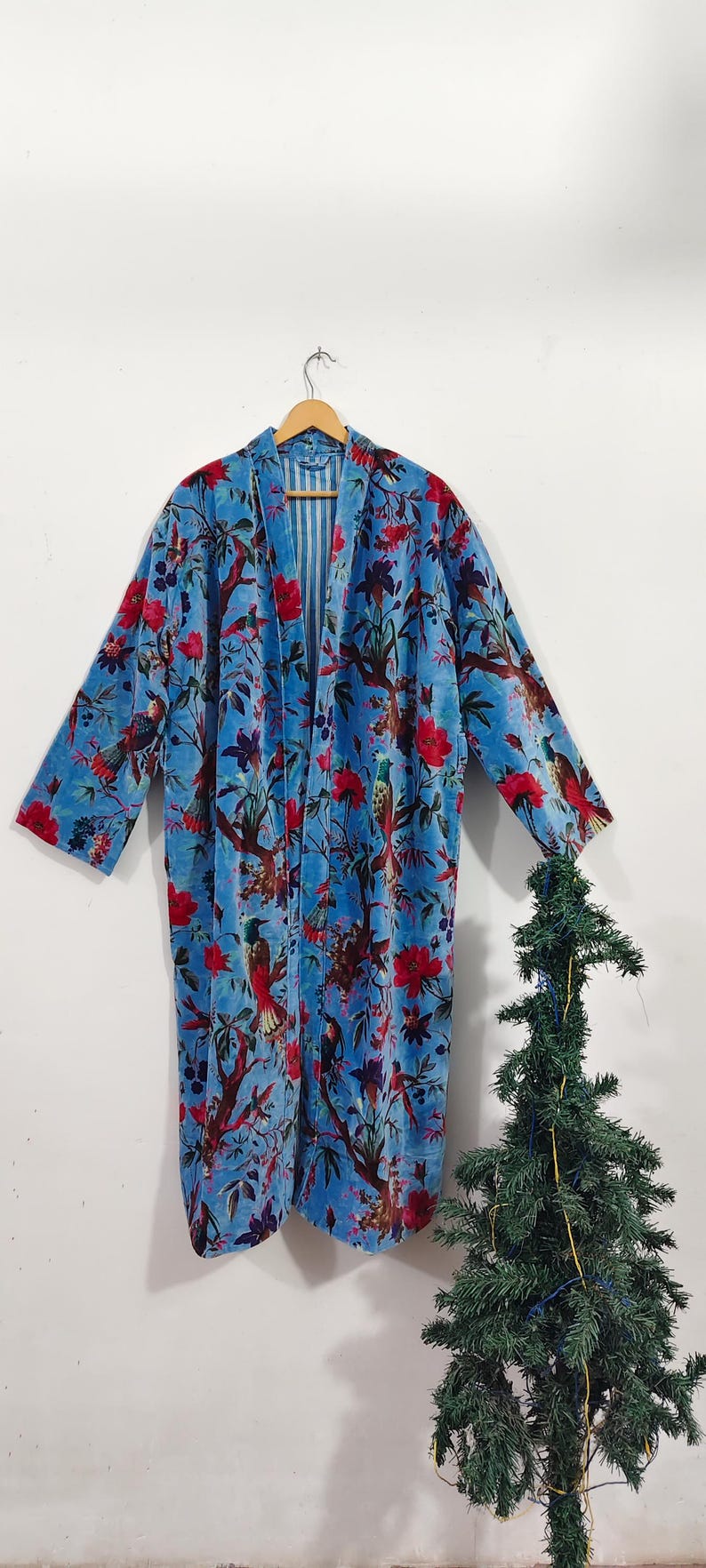 May include: A long, open-front robe in a vibrant blue hue, adorned with a detailed floral and bird pattern in red and brown. The robe is hanging on a wooden hanger against a white background, showcasing its flowing design.
