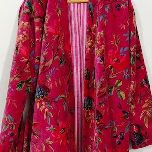 Puede incluir: Bata larga y abierta de color magenta vibrante, adornada con un estampado floral y de p&aacute;jaros en tonos rojos, verdes, azules y dorados. La bata presenta un forro interior a rayas y se exhibe en una percha de madera.
