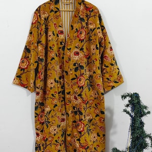 Puede incluir: Bata estilo kimono con estampado floral amarillo mostaza. La bata presenta un estampado floral a gran escala en rojo, naranja y verde. El forro interior tiene un estampado de rayas. La bata est&aacute; colgada de una percha de madera.