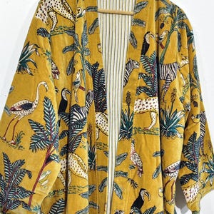 May include: Mustard yellow velvet kimono with a jungle animal print. The open front robe features a pattern of zebras, leopards, toucans, and other birds and foliage. The interior lining is white with vertical stripes.