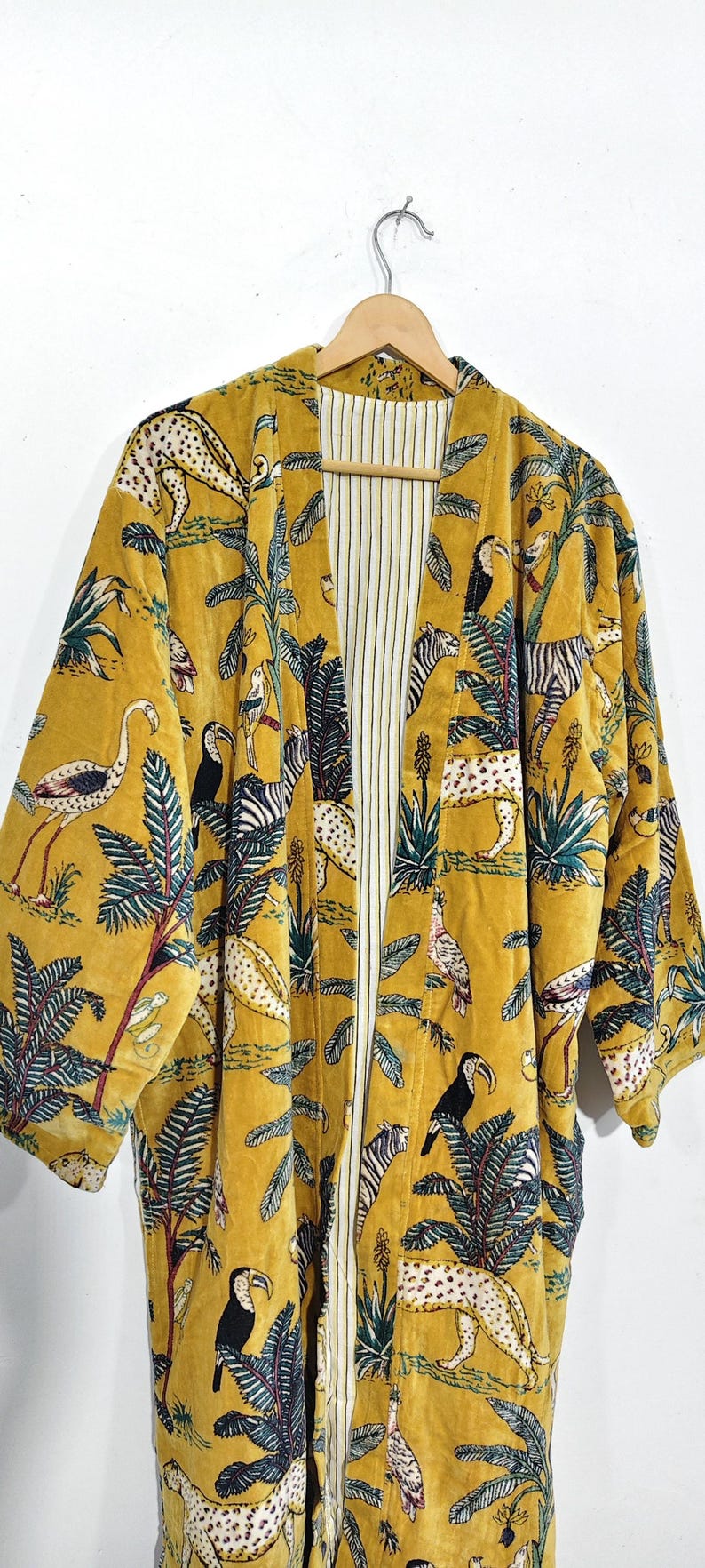 May include: Mustard yellow velvet kimono with a jungle animal print. The open front robe features a pattern of zebras, leopards, toucans, and other birds and foliage. The interior lining is white with vertical stripes.