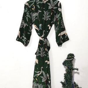 May include: Dark green robe with a jungle print featuring leopards, palm trees, and birds. The robe has a tie closure and three-quarter sleeves. The robe is hanging on a wooden hanger.