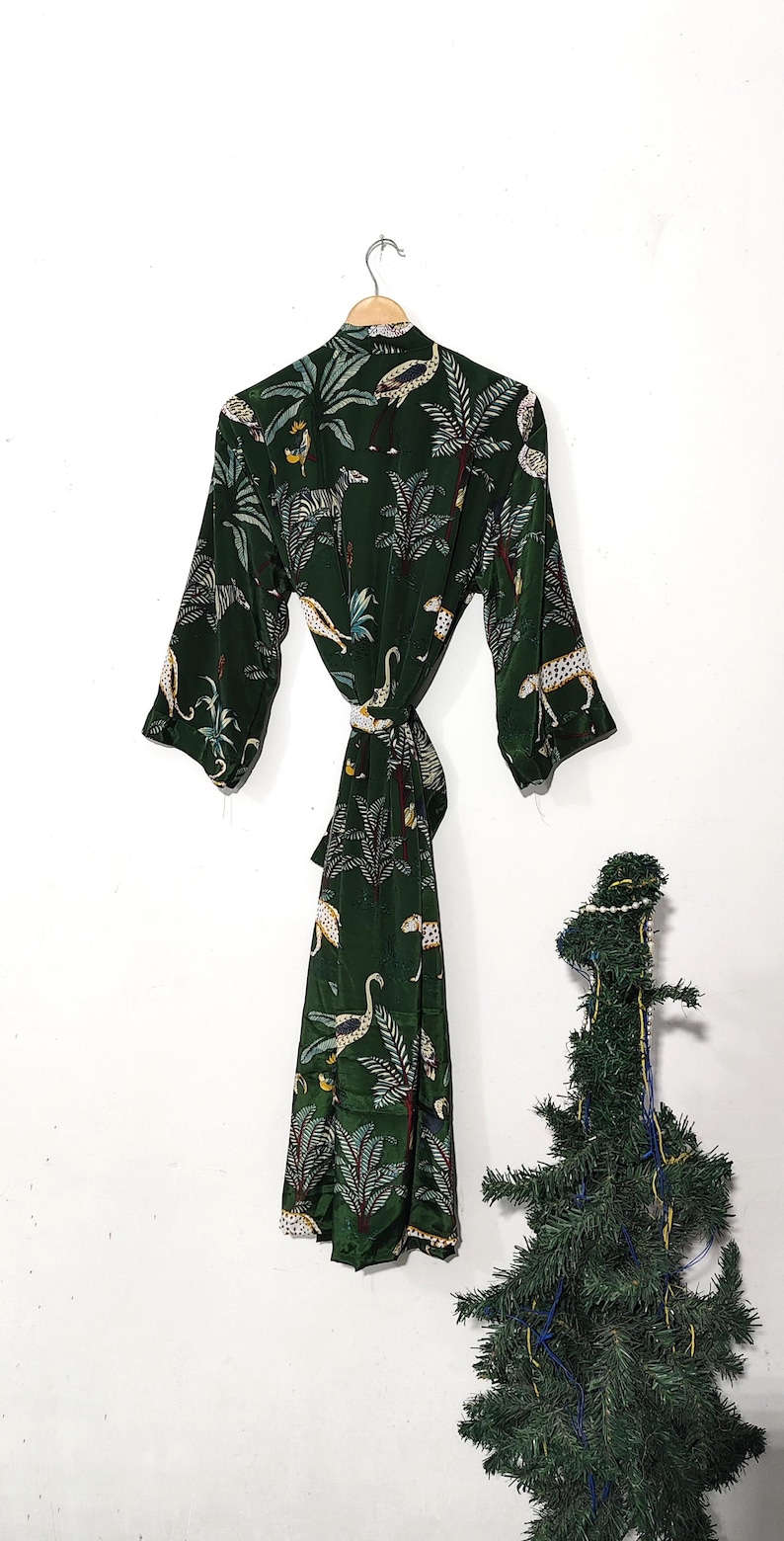 May include: Dark green robe with a jungle print featuring leopards, palm trees, and birds. The robe has a tie closure and three-quarter sleeves. The robe is hanging on a wooden hanger.