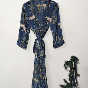 May include: A blue robe with a jungle print featuring leopards and palm trees. The robe is hanging on a wooden hanger and tied at the waist. The fabric has a silky sheen.