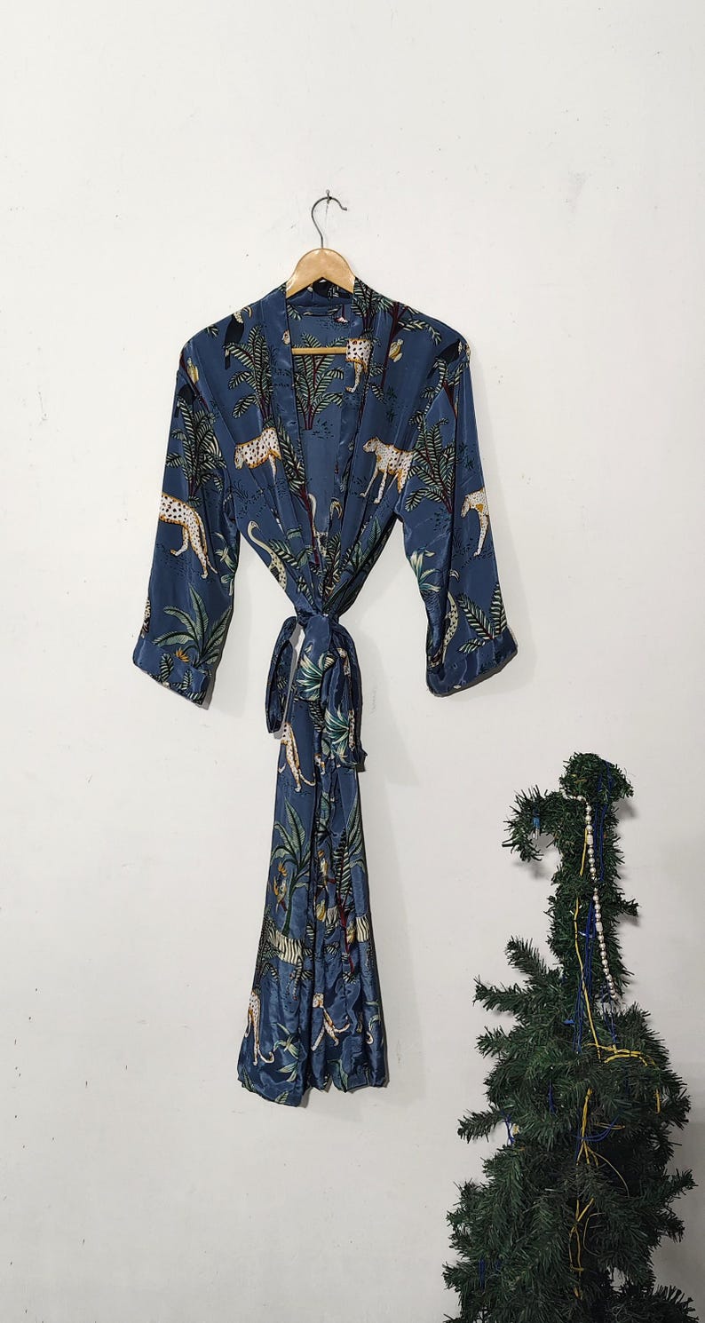 May include: A blue robe with a jungle print featuring leopards and palm trees. The robe is hanging on a wooden hanger and tied at the waist. The fabric has a silky sheen.