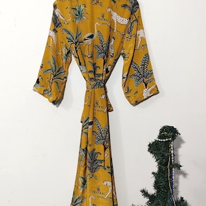 May include: Mustard yellow robe with a jungle print featuring leopards, birds, and palm trees. The robe has a tie waist and three-quarter sleeves. The robe is hanging on a wooden hanger.
