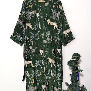 May include: A dark green kimono-style robe with a jungle-themed pattern. The robe features a repeating design of leopards, zebras, and tropical foliage. The robe is hanging on a wooden hanger.