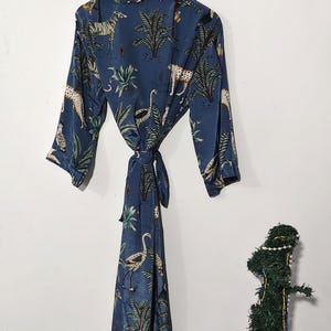May include: A blue robe with a jungle animal print, including zebras, leopards, and birds, hangs on a wooden hanger. The robe is tied at the waist with a matching fabric belt. The robe is made of a silky material.