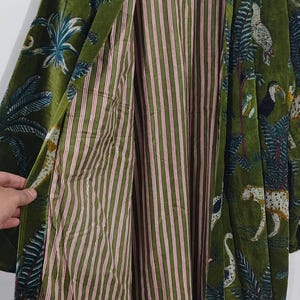 May include: Green velvet robe with a tropical print featuring toucans, leopards, and palm trees. The robe's interior has a striped pattern in shades of green and red. A stylish, long-sleeved garment.