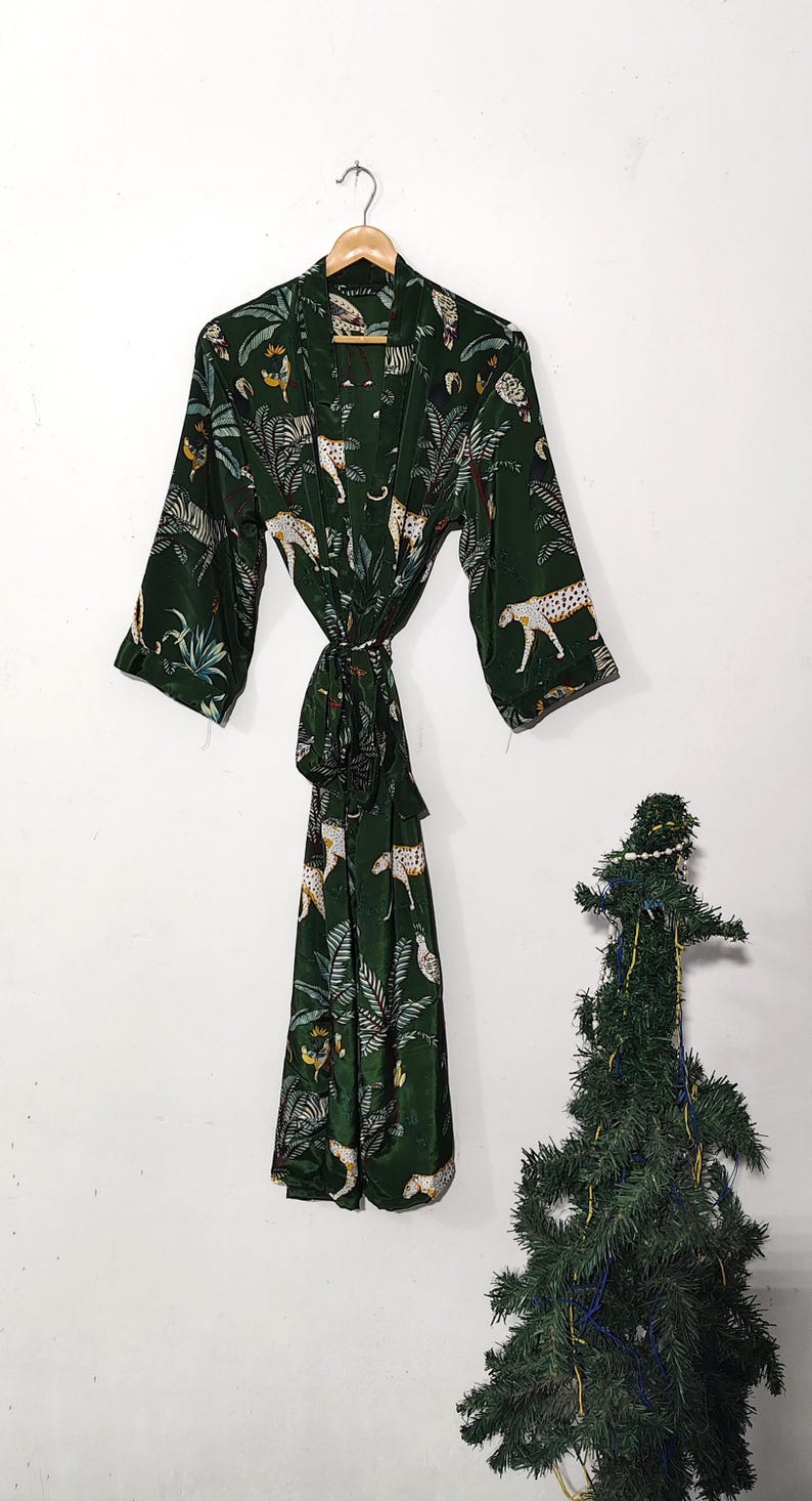 May include: A dark green robe with a jungle and leopard print. The robe is hanging on a wooden hanger against a white wall. The robe has long sleeves and a matching tie belt.