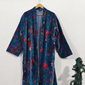 May include: A long, open-front robe in a teal blue hue, adorned with a vibrant floral pattern in red and green. The robe features long sleeves and a striped inner lining. It is hanging on a wooden hanger.