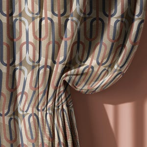 May include: Close-up of a patterned fabric with a repeating design of interlocking shapes in shades of beige, brown, and navy blue. The fabric is draped, showing folds and texture. The background is a solid, warm-toned wall.