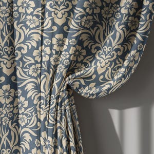 May include: A section of a blue curtain with a beige floral pattern. The curtain is gathered and draped, revealing the intricate design of flowers and swirling leaves. The fabric is textured, and the pattern is repeated throughout the curtain.