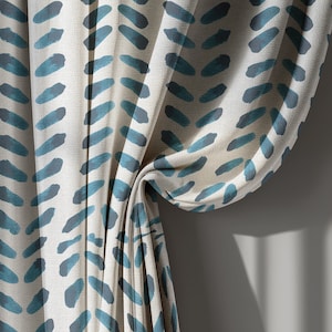 May include: Cream-colored curtain with a repeating pattern of teal brushstrokes. The fabric is draped, revealing the texture and design. The curtain is hanging against a neutral-colored wall, with shadows.