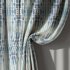 May include: Curtains with a repeating pattern of vertical blue and white shapes. The fabric is draped, showing folds and texture. The color palette is cool, with shades of blue and white.