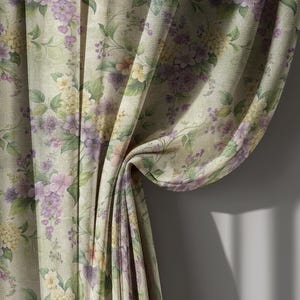 May include: Floral patterned curtain fabric. The fabric features a repeating pattern of purple, yellow, and green flowers and leaves on a light green background. The curtain is draped, showing the texture and folds of the fabric.