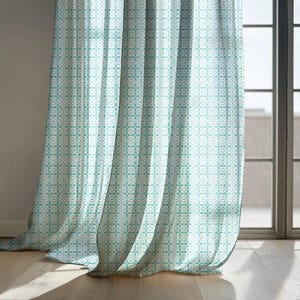 May include: Light blue and white patterned curtains hanging in front of a window. The curtains have a repeating geometric design. The curtains are made of a lightweight fabric and are partially see-through, allowing sunlight to filter through.