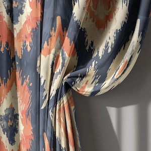 May include: Curtains with a navy blue, peach, and cream ikat pattern. The fabric is draped, showing the design's repeating geometric shapes. The curtains are made of a lightweight material.