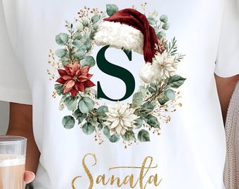 Camiseta navideña con la inicial S de Papá Noel, corona floral, gorro de Papá Noel y elegante escritura para las fiestas.