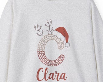 Suéter navideño personalizado de Clara con inicial C tejida, gorro de Papá Noel y sudadera navideña con astas de reno.
