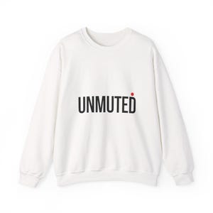Puede incluir: Sudadera blanca de cuello redondo con la palabra "UNMUTED" impresa en negro, con un punto rojo encima de la "d". La sudadera tiene mangas largas y un corte holgado.