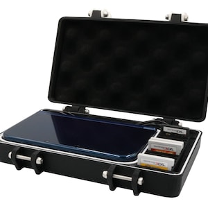 May include: Black hard case with a blue handheld gaming device and three game cartridges. The case has a foam interior and metal latches. The handheld device is open and ready to use.
