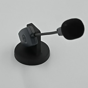 May include: A black desktop microphone with a round base and a flexible arm. The microphone has a small, rounded head covered in black fabric. The base and arm are also black, creating a sleek, modern appearance.