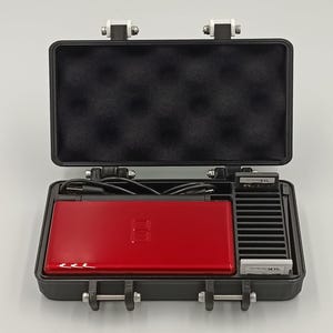May include: A red Nintendo DS Lite console inside a black carrying case. The case is open, revealing the console, game cartridges, and a charging cable. The case has a foam interior and metal latches.
