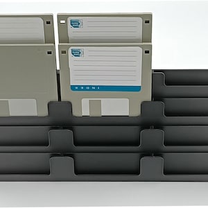 May include: A black plastic organizer holding several 3.5-inch floppy disks. The disks are light gray with white labels and are arranged in a tiered, stepped design. The organizer has multiple slots.