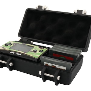 May include: Black, open, hard-shell case with a camouflage-patterned handheld game console and game cartridges. The case has a foam-padded interior and metal latches. The game console is green, brown, and tan.