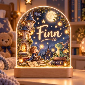 May include: An arched acrylic night light with a wooden base featuring a fantasy illustration of a child and a green dragon sitting among books and a castle. The name Finn is written in white script in the center under a full moon and stars.