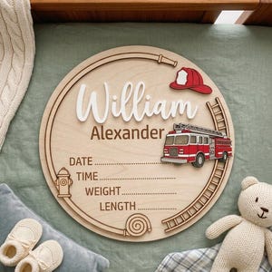 May include: A circular wooden birth announcement sign featuring the name William Alexander in white script, a red fire truck, a red fire helmet, a fire hydrant, and a hose. The sign includes engraved lines for date, time, weight, and length.
