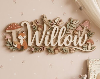 Può includere: Una targa decorativa da parete con il nome Willow in caratteri corsivi bianchi, circondata da elementi boschivi in 3D tra cui una volpe, vari funghi, ghiande e rami frondosi in tonalità terra e rosa tenue.
