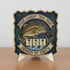 Puede incluir: Placa de madera con temática de pesca con una ilustración de lubina, el texto "FISH CAUGHT THIS YEAR" y el número "162". La placa está soportada por un soporte de madera y presenta el texto "HOOKED BY SMITH".
