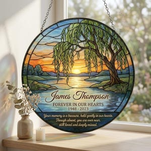 May include: Round stained glass memorial with a willow tree scene, sunset, and water. Text reads "James Thompson Forever in Our Hearts 1948-2023". Includes the quote: "Your memory is a treasure, held gently in our hearts."