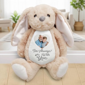 Puede incluir: Un conejo de peluche de color beige claro, con orejas largas y una nariz gris. El conejo tiene un parche blanco en forma de corazón en el pecho con una foto de un hombre y un niño. El texto "I'm Always With You" está impreso debajo.