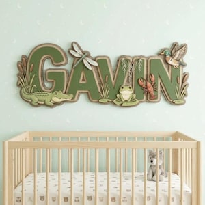 Op de afbeelding: Een decoratief houten naambord voor aan de muur met de naam GAVIN in grote groene letters. Het bord bevat gedetailleerde uitsparingen van een groene alligator, een libel, een kikker, een rode rivierkreeft en een wilde eend met riet.