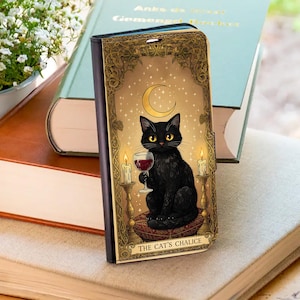 Op de afbeelding: Zwarte telefoonhoes met een zwarte kat die een glas rode wijn, een halve maan en kaarsen vasthoudt. De hoes heeft een gouden, sierlijke lijst en de tekst "THE CAT'S CHALICE".