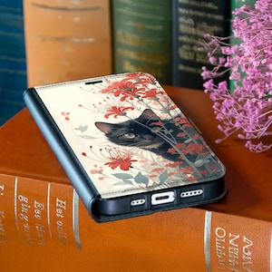 Puede incluir: Funda de teléfono con gato negro y diseño floral. La funda presenta un gato negro asomándose entre flores rojas y hojas verdes sobre un fondo crema. La funda es negra con cierre magnético y soporte para teléfono.
