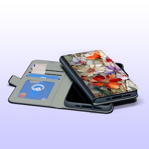 May include: A smartphone case with a floral design featuring red, orange, white, and purple flowers. The case is open, revealing a phone and a section for cards and cash. The case is gray and black.