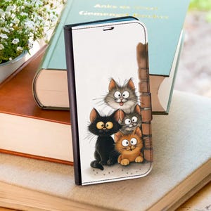 Puede incluir: Una funda de teléfono blanca con una ilustración de dibujos animados de cuatro gatos. Los gatos son de varios colores, incluyendo negro, gris y naranja, con ojos expresivos y poses juguetonas. La funda tiene un borde negro y un diseño de pared de ladrillo.