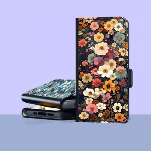 Puede incluir: Una funda floral para teléfono con un fondo oscuro y flores coloridas en tonos rosa, naranja, amarillo y blanco. La funda se cierra con un cierre magnético negro. Se ven dos fundas de teléfono adicionales.