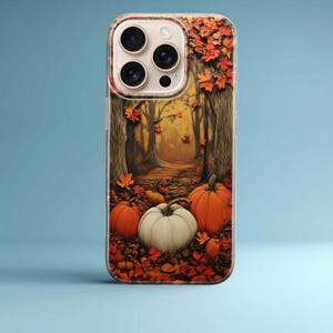 May include: A clear smartphone case featuring a printed design of an autumn forest scene with orange and white pumpkins resting on a ground covered in fallen red and orange leaves, set against a backdrop of tall trees and a path leading into the woods.